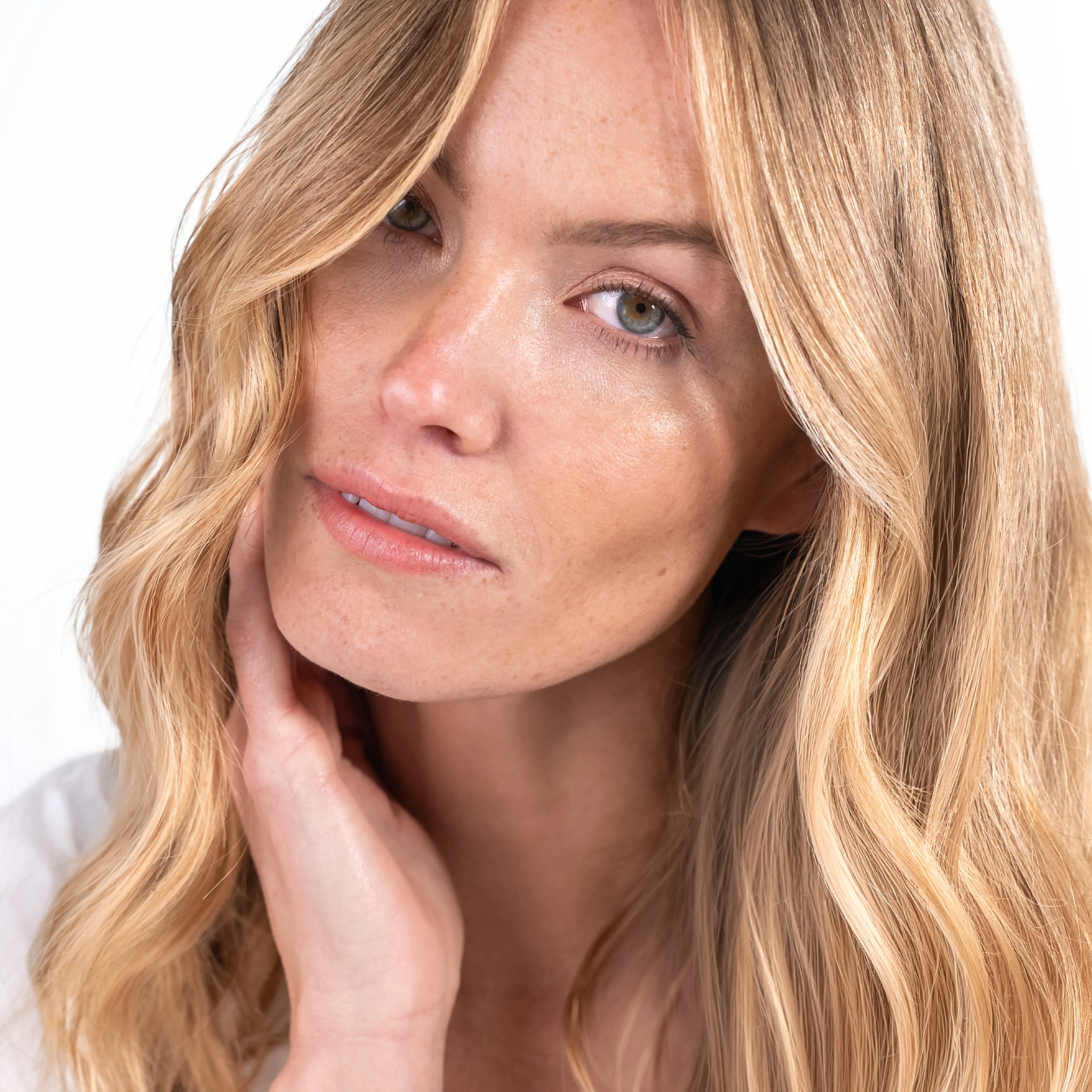 Portrait einer blonden Frau mit weichen Wellen und nat&uuml;rlichem Glow auf hellem Hintergrund.